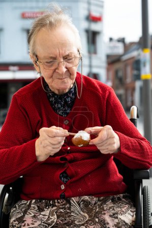Foto de 84 años mujer mayor comiendo un donut mientras está sentada en una silla de ruedas, Tienen, Bélgica - Imagen libre de derechos