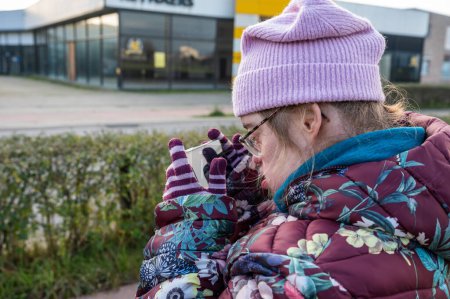 Foto de Mujer feliz de 40 años con el Síndrome de Down en ropa de invierno usando un teléfono inteligente, Flandes, Tienen, Bélgica - Imagen libre de derechos