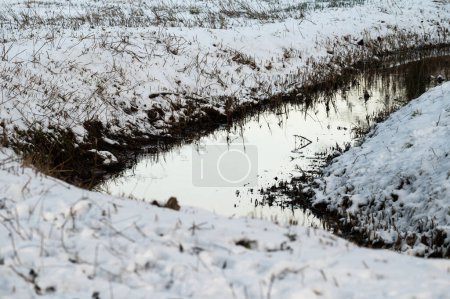 The bending Molenbeek creek through the snowy meadows in Jette, Brussels, Belgium