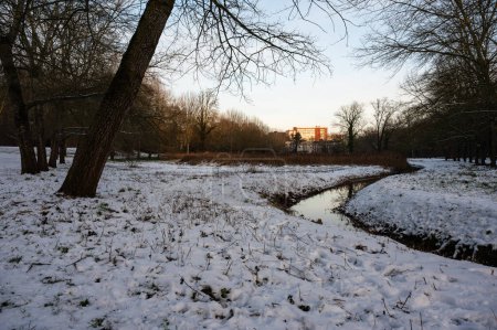 The bending Molenbeek creek through the park, covered with snow at dusk, Jette, Brussels, Belgium