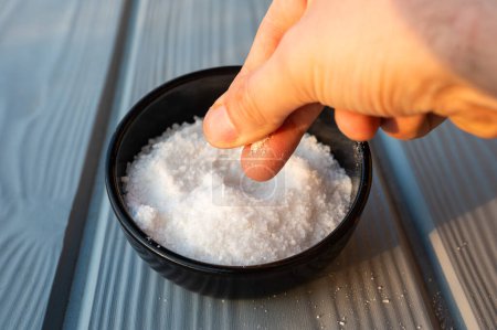 Cook's hand taking coarsed sea salt out of a black bowl, Brussels, Belgium
