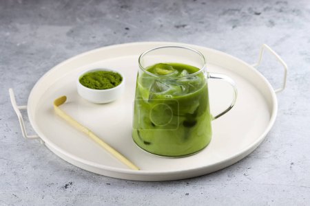Photo for Serving tray with iced matcha latte, a bowl of matcha powder and matcha spoon. Refreshing antioxidant drink made of ground powder of green tea leaves mixed with milk and ice cubes in a transparent cup. Matcha latte antioxidant detoxing natural drink. - Royalty Free Image