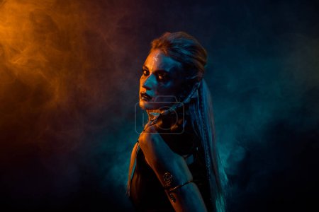 Téléchargez les photos : Photo de profil de terrifiant valkyrie païenne femme regard effrayant orange bleu lumières de couleur isolé sur fond sombre. - en image libre de droit