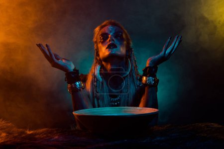 Foto de Foto de cuerpo sangriento arte vikinga mujer orar espíritus muertos poción cuenco naranja azul luces niebla aislado sobre fondo oscuro. - Imagen libre de derechos