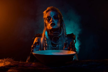 Téléchargez les photos : Portrait du nord mythologie sorcier fille préparer bataille élixir orange bleu lumières brouillard isolé sur fond sombre. - en image libre de droit