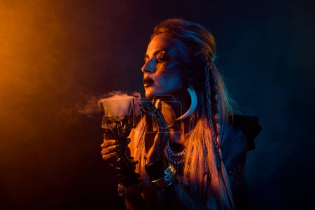 Foto de Retrato de demonio pagano mago chica celebrar olor poción taza naranja luz niebla aislada sobre fondo oscuro. - Imagen libre de derechos