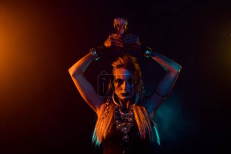 Portrait of dangerous fearless valkyrie girl hold potion cup above head orange lights isolated on dark background.