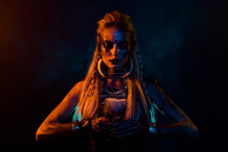 Foto de Foto de misteriosa chica conjuradora vikinga preparar inmortalidad elixir luces naranjas aisladas sobre fondo de color negro. - Imagen libre de derechos