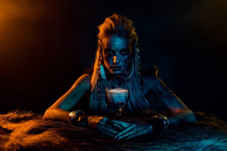 Foto de Foto de misteriosa mitología vikinga hechicera mujer sostiene elixir taza luces amarillas aisladas sobre fondo de color negro. - Imagen libre de derechos