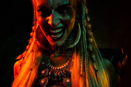 Foto de Foto de señora misteriosa enojada loca usar ropa vikinga que muestra los dientes mordiendo fondo de color naranja oscuro aislado. - Imagen libre de derechos