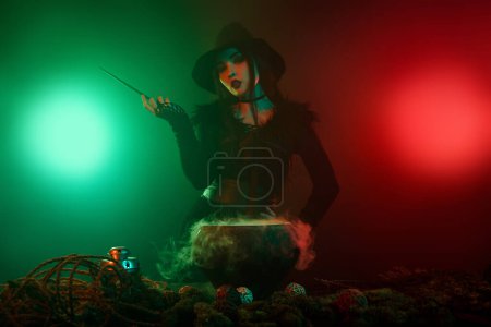 Foto de Foto de poderoso mago haciendo hechizo mágico oscuro con caldero de poción de varita sobre fondo de neón niebla. - Imagen libre de derechos