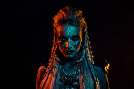 Téléchargez les photos : Portrait de dangereuse femme viking intrépide regard maléfique bleu orange effet de lumière isolé sur fond noir. - en image libre de droit