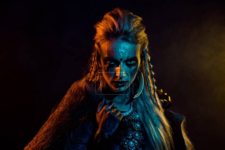 Foto de Retrato de chica vikinga misteriosa despiadada mirada enojada luces azules amarillas niebla aislada sobre fondo de color negro. - Imagen libre de derechos