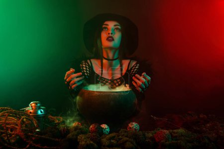 Foto de Foto de bruja medieval oscura haciendo ritual con poción de caldero hablar con espíritus fantasma sobre fondo de neón. - Imagen libre de derechos
