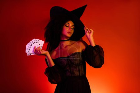 Photo for Gorgeous lady bewitched people on halloween night do dark spell with poker playing cards over red background. - Royalty Free Image