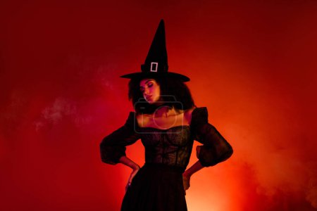 Foto de Foto del malvado diablo dama bruja toque vestido gótico medieval para Halloween evento Sabbath sobre fondo rojo. - Imagen libre de derechos