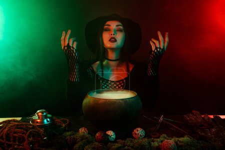 Photo for Photo of dark lady alchemist necromancer doing ritual with cauldron speak with ghosts spirits over neon background. - Royalty Free Image