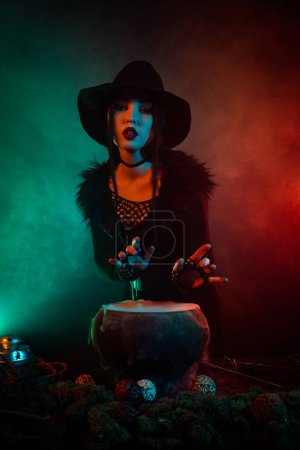 Photo for Photo of powerful evil witch cooking potion boiling in cauldron on halloween night over mist neon background. - Royalty Free Image