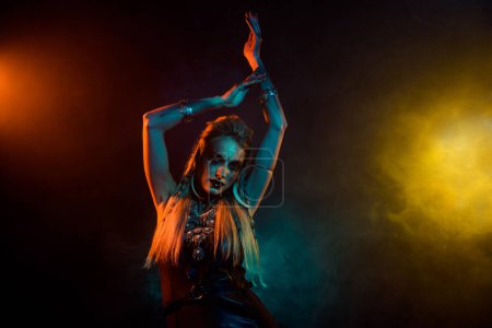 Foto de Foto de atractiva dama misteriosa salvaje usar ropa vikinga disfrutando de danza ritual aislado humo naranja fondo. - Imagen libre de derechos