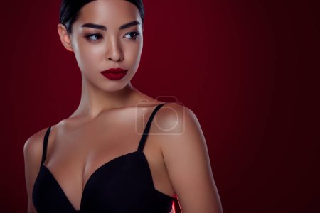 Foto de Foto de impresionante mujer asiática femme fatale look vacío espacio negro sujetador hombros de aislado de color rojo oscuro fondo. - Imagen libre de derechos