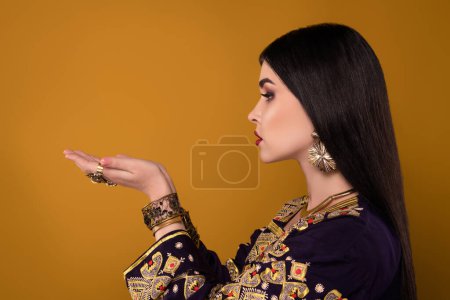 Téléchargez les photos : Photo de riche dame arabe tenant la main montrent la publicité traditionnelle promo ethnique sur l'espace vide pastel. - en image libre de droit