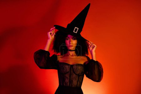 Téléchargez les photos : Photo de stupéfiante dame magnifique se préparer pour Halloween costume de robe tactile de carnaval comme sorcière maléfique sur fond rouge. - en image libre de droit