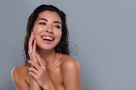 Téléchargez les photos : Photo de belle asiatique jeune fille toucher doux peau lisse joue spa salon épaules off isolé fond de couleur grise. - en image libre de droit
