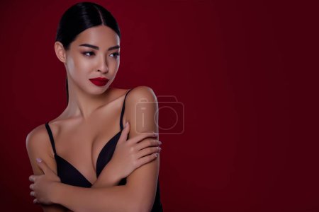Foto de Foto de mujer joven asiática femme fatale look espacio vacío abrazándose a sí mismos hombros de fondo de color rojo oscuro aislado. - Imagen libre de derechos