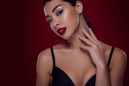 Foto de Foto de chica joven asiática femme fatale touch seductor cuello negro sujetador hombros fuera aislado color rojo oscuro fondo. - Imagen libre de derechos