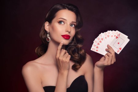 Foto de Foto de elegante señora jugador de póquer con clase mantener las cartas cara táctil pensando en la estrategia de la suerte ganar sobre fondo oscuro. - Imagen libre de derechos