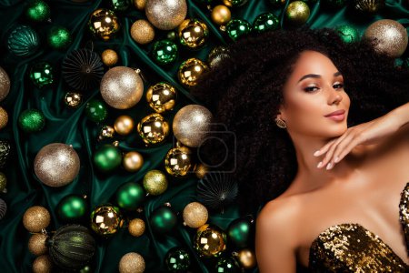 Photo for Top view closeup portrait of sensual lady laying on decorated xmas baubles background covered emerald silk texture. - Royalty Free Image