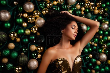 Téléchargez les photos : Portrait de vue de dessus de dame étonnante posant couché sur la texture soyeuse émeraude décorée de boules de paillettes arbre de Noël. - en image libre de droit