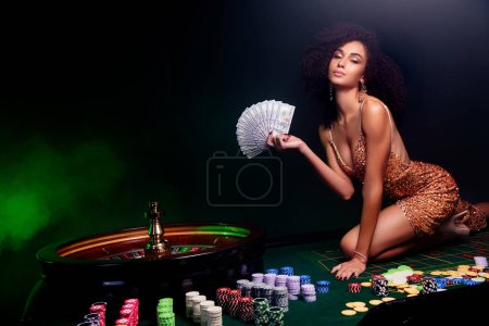 Téléchargez les photos : Photo de superbe dame élégante sur la table de poker tenir le prix des billets dans le club de partie de jeu avec des effets de filtre au néon. - en image libre de droit