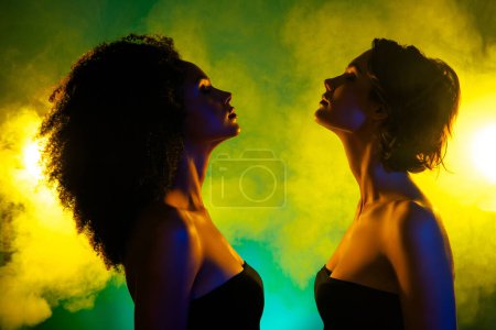 Photo for Photo of two girls over mist bright shine background dance in modern futuristic night club. - Royalty Free Image