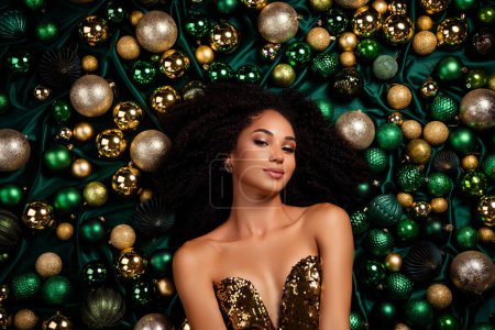 Photo for Professional studio portrait of attractive woman laying between xmas event golden tree baubles luxury background. - Royalty Free Image