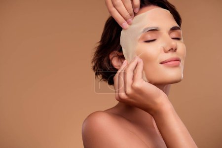 Photo for Photo of lady touch applying face sheet mask for silky skin new daily morning routine on beige color background. - Royalty Free Image