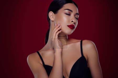Foto de Foto de hermosa chica joven asiática femme fatale ojos cerrados toque cuello hombros fuera aislado color rojo oscuro fondo. - Imagen libre de derechos