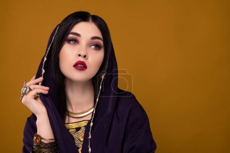 Foto de Foto de misteriosa dama viajera beduina del desierto usando magia para coquetear rico sultán sobre copyspace pastel. - Imagen libre de derechos