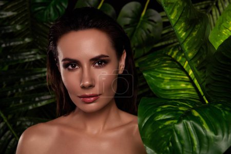 Téléchargez les photos : Portrait de charmante jeune femme modèle applique un shampooing pour les cheveux propres et humides dans les feuilles tropicales de la forêt tropicale. - en image libre de droit