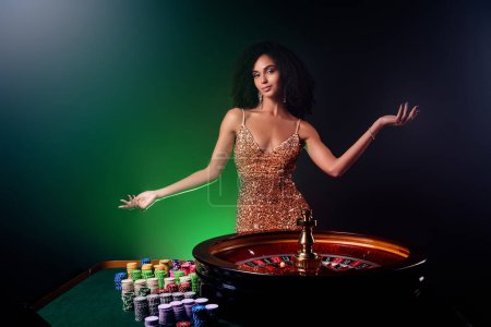 Foto de Foto de elegante dama atractiva en vestido de oro mostrando publicidad vip poker club sobre fondo de filtro oscuro. - Imagen libre de derechos