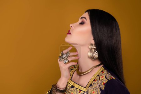 Téléchargez les photos : Photo d'élégante dame magnifique reine arabique en vêtements nationaux toucher le cou sur fond pastel. - en image libre de droit