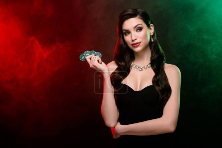 Foto de Elegante elegante rica dama rica jugador de póquer profesional mantenga fichas buscar competidores sobre fondo de neón oscuro niebla. - Imagen libre de derechos
