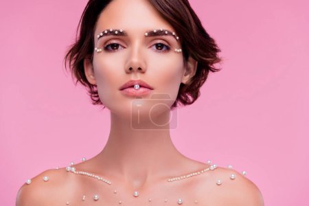 Téléchargez les photos : Photo attrayant magnifique dame mordre perles blanches annoncer magasin de bijoux sur fond de couleur rose. - en image libre de droit
