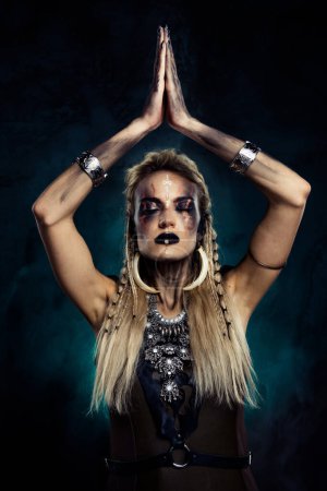 Téléchargez les photos : Photo de dame puissante viking chaman tribal lever la main appel parler avec des ancêtres effrayant démon sur fond de brume. - en image libre de droit