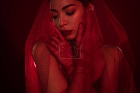 Téléchargez les photos : Photo de jeune femme asiatique femme fatale touch visage taquinant sexy mariée épaules off isolé fond de couleur rouge foncé. - en image libre de droit
