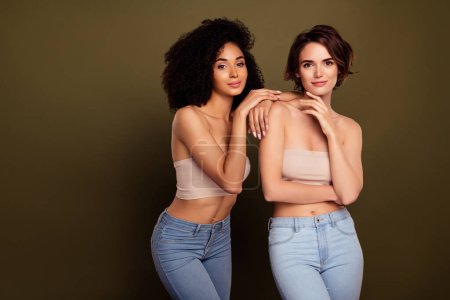Foto de Dos apasionados modelos de señora tocan hombro cuando se visten tops en procedimientos de spa aislados sobre fondo de color caqui. - Imagen libre de derechos