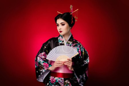 Téléchargez les photos : Photo de glamour asiatique dame anime théâtre personnage habillé kimono tenir ventilateur isolé sur fond de couleur dégradé rouge. - en image libre de droit
