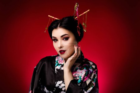 Foto de Foto de elegante señora vestida kimono negro ropa coreana mano tacto cara aislada en rojo degradado color fondo. - Imagen libre de derechos