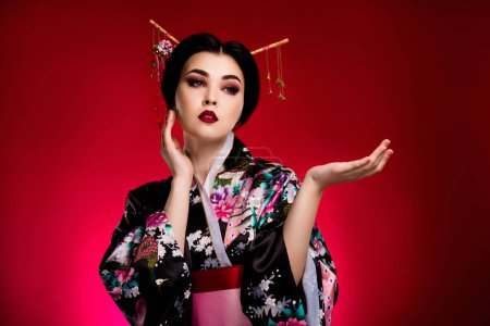 Téléchargez les photos : Photo de sophistiquée asiatique dame tenir la main démontrer annonces sur festival culturel japonais sur fond rouge vif. - en image libre de droit