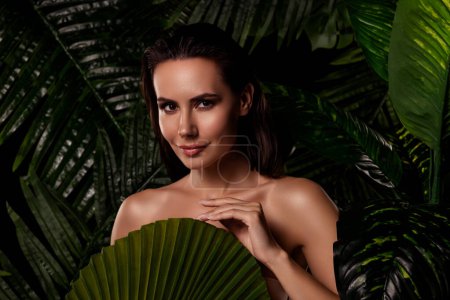 Téléchargez les photos : Photo de séduisante jolie femme épaules nues couvrant le corps feuille de palmier à l'extérieur forêt tropicale. - en image libre de droit